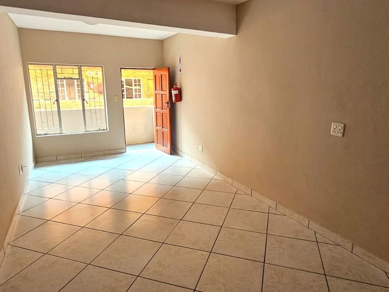 An empty, neutrally painted living area featuring tiled flooring, natural light from the window, and direct access to an outdoor space.