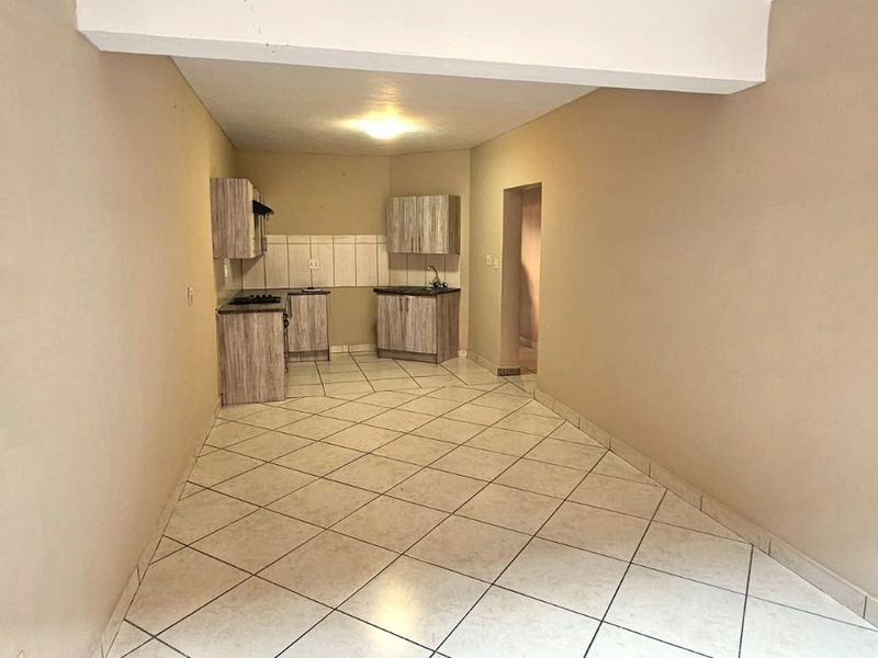 An empty open-plan living and kitchen area featuring tiled flooring and basic built-in cabinetry with a hob and sink.