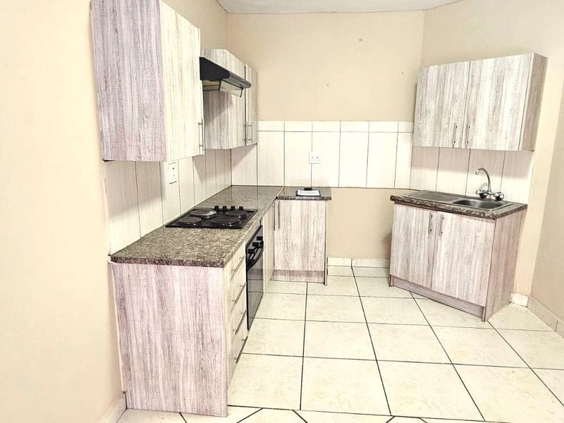 Compact kitchen featuring light wood-grain cabinetry, granite-look countertops, built-in oven and hob, and neutral ceramic floor tiling.