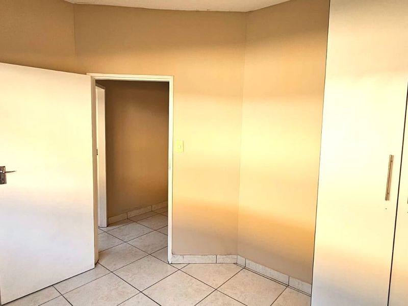 A clean, empty bedroom featuring neutral wall tones, tiled flooring, and built-in cupboards, offering a versatile space ready for personalization.
