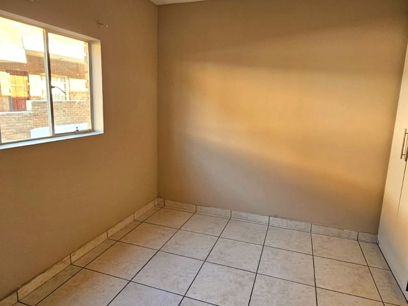 A clean, empty bedroom featuring neutral tiled flooring, a built-in wardrobe, and natural light from a large window.