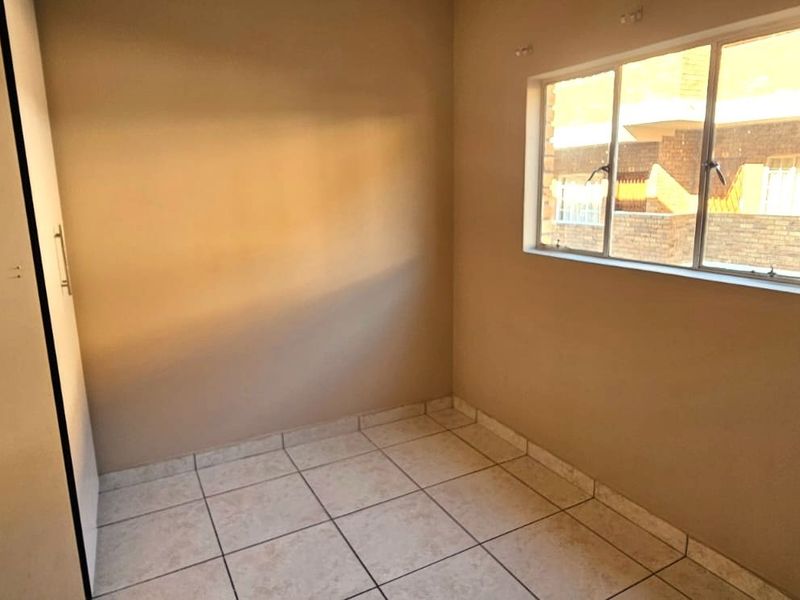 A compact, empty bedroom featuring tiled flooring, a built-in wardrobe, and a window providing natural light.