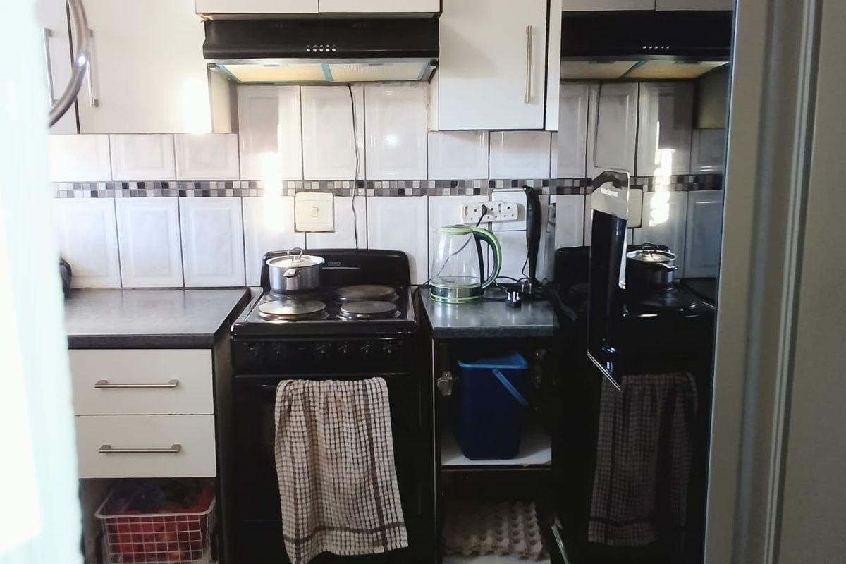 Compact kitchen featuring built-in cabinetry, a tiled backsplash, and a freestanding electric stove with an integrated extractor fan.