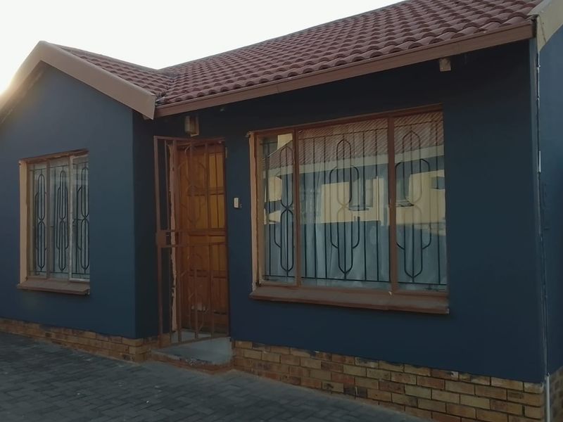 Front elevation of a residential house featuring dark painted walls, a tiled roof, and security gates over the entrance and windows.