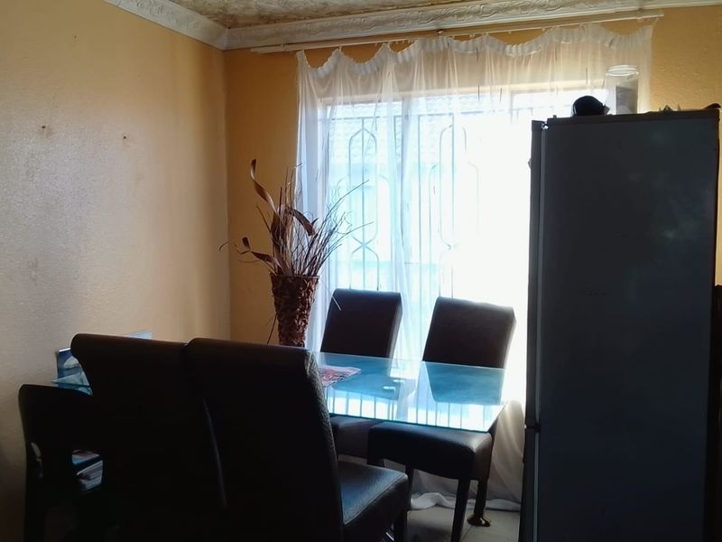 A dining area featuring a window with security bars and decorative ceiling cornicing, requiring cosmetic updates to improve the overall aesthetic.