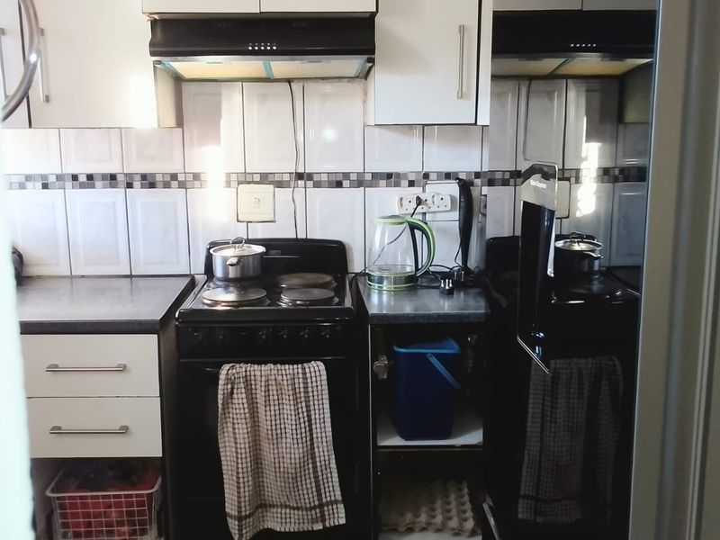 Compact kitchen featuring built-in cabinetry, a tiled backsplash, and a freestanding electric stove with an integrated extractor fan.
