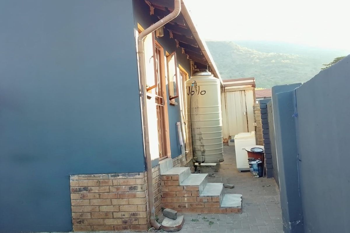Rear exterior view of the property featuring a paved walkway, brick steps, and a water storage tank against a painted wall.