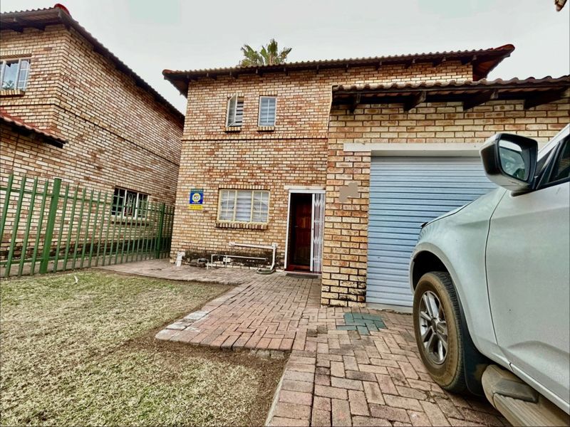 Front exterior view of a face brick house featuring a paved driveway, single garage, and security gate entrance.