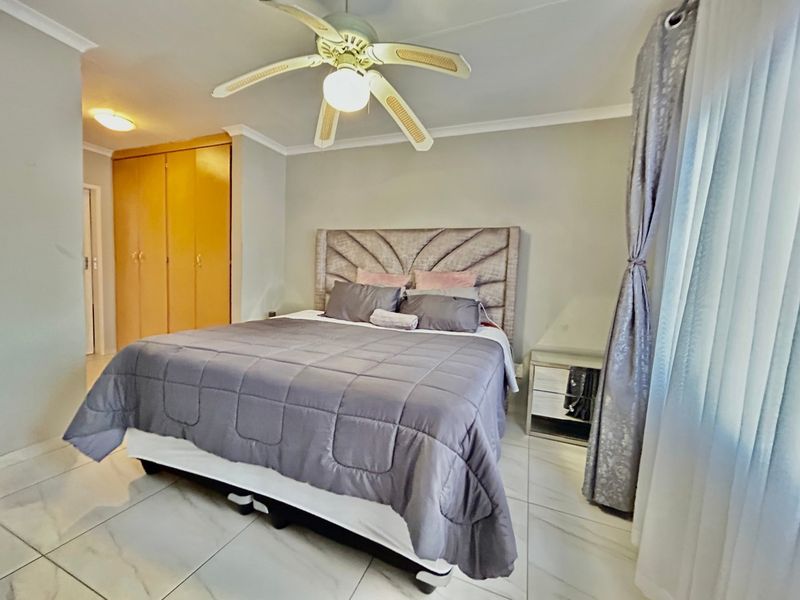 A bedroom featuring tiled flooring, a ceiling fan, and built-in cupboards, providing a functional and neutral living space.