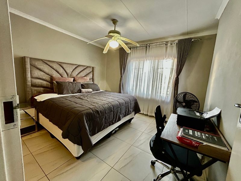 A well-maintained bedroom featuring neutral tiled flooring, a central ceiling fan, and large windows with fitted curtain rails.