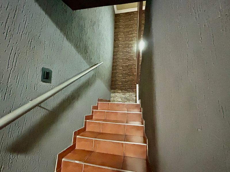 A staircase featuring tiled steps, a metal handrail, and a decorative stone veneer accent wall.