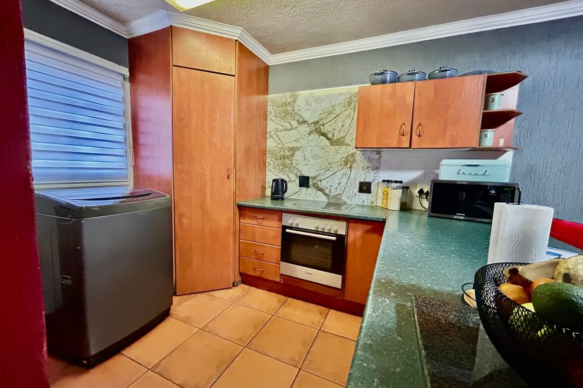 A functional kitchen featuring wood-finish cabinetry, green laminate countertops, built-in oven, and tiled flooring, offering a practical layout for daily use.