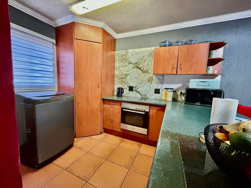 A functional kitchen featuring wood-finish cabinetry, green laminate countertops, built-in oven, and tiled flooring, offering a practical layout for daily use.