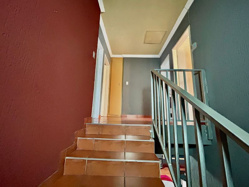 A functional hallway featuring a tiled staircase with a metal handrail, leading to an upper level with built-in storage.