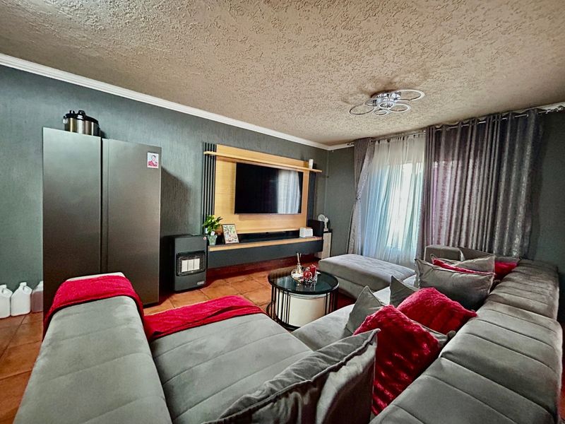 A comfortable living room featuring a built-in media unit, textured ceiling, and tiled flooring, providing a functional space for relaxation.