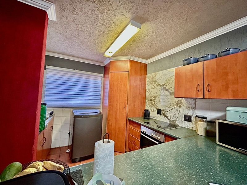 A functional kitchen featuring wood-finish cabinetry, green laminate countertops, a built-in oven with hob, and tiled backsplash detailing.