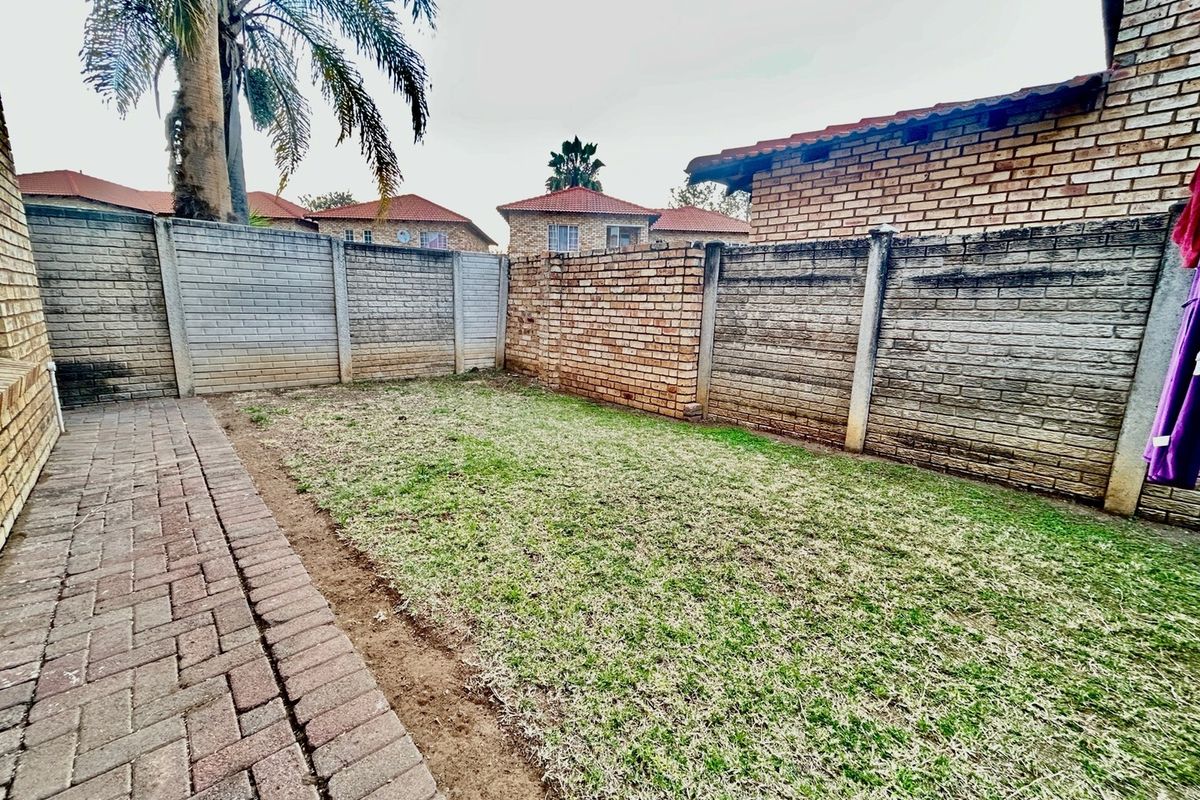A private rear garden area featuring a paved walkway, a small lawn, and enclosed by brick boundary walls.