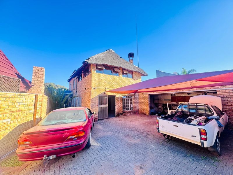 Front exterior view of a face brick house featuring a thatch roof, paved driveway, and a double garage with a shade sail.