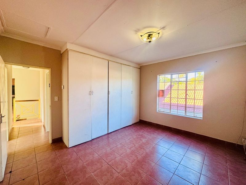 A vacant bedroom featuring built-in cupboards, tiled flooring, and a window with security bars, offering a functional space ready for personalization.
