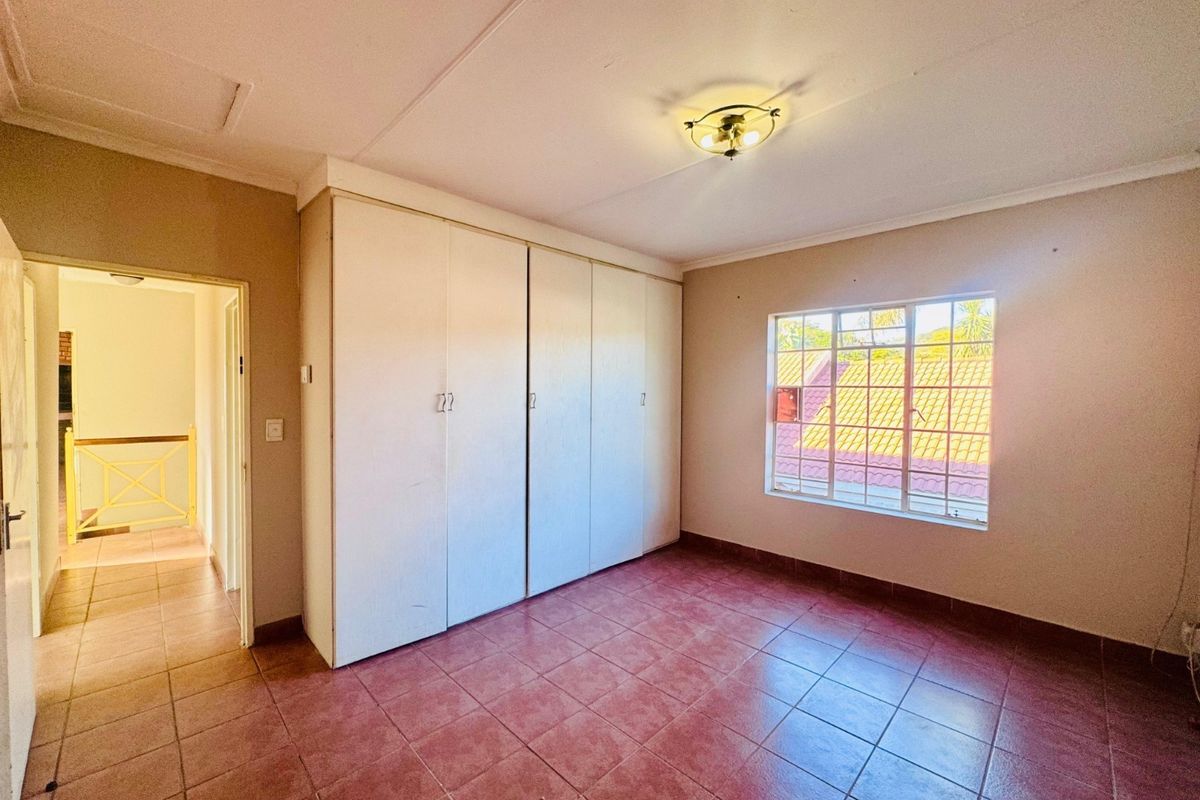 A vacant bedroom featuring built-in cupboards, tiled flooring, and a window with security bars, offering a functional space ready for personalization.
