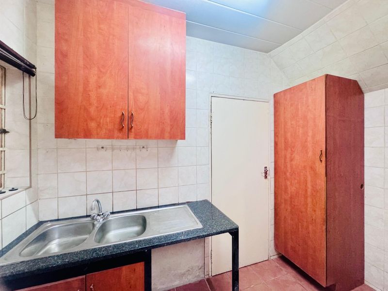 A functional scullery area featuring double bowl stainless steel sink, granite countertops, and built-in laminate cabinetry with tiled wall finishes.