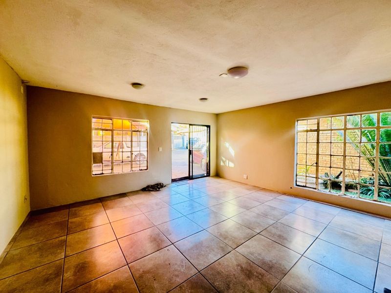 An empty living room featuring tiled flooring, steel-framed windows, and a sliding glass door providing access to the exterior.