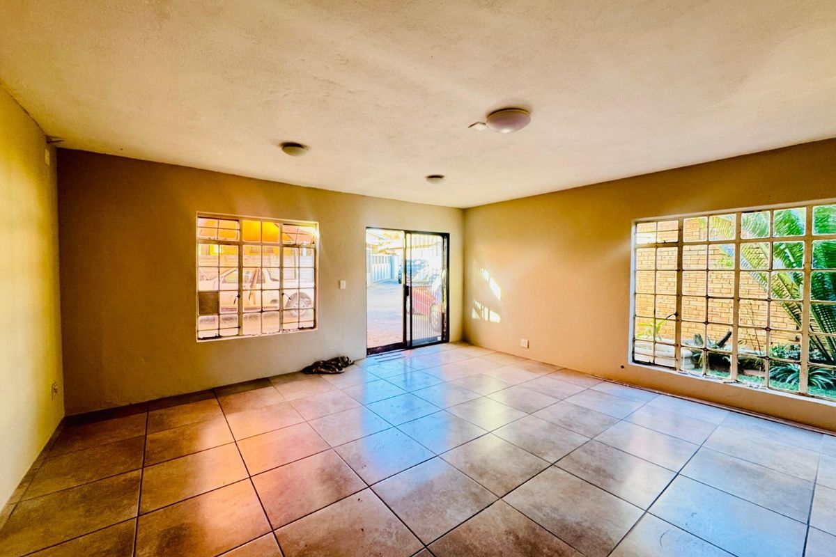 An empty living room featuring tiled flooring, steel-framed windows, and a sliding glass door providing access to the exterior.