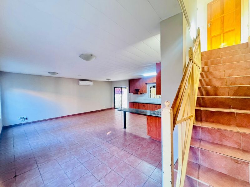 Spacious open-plan living area featuring tiled floors, a functional kitchen with built-in cabinetry, and a staircase leading to the upper level.