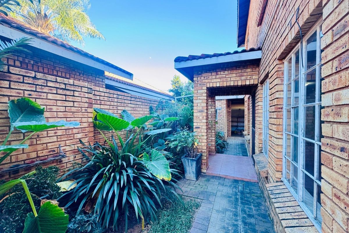 A side walkway featuring face brick walls, a covered entrance, and established garden beds along the exterior of the house.