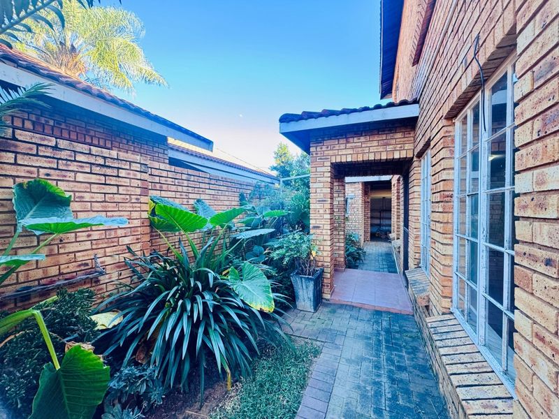 A side walkway featuring face brick walls, a covered entrance, and established garden beds along the exterior of the house.