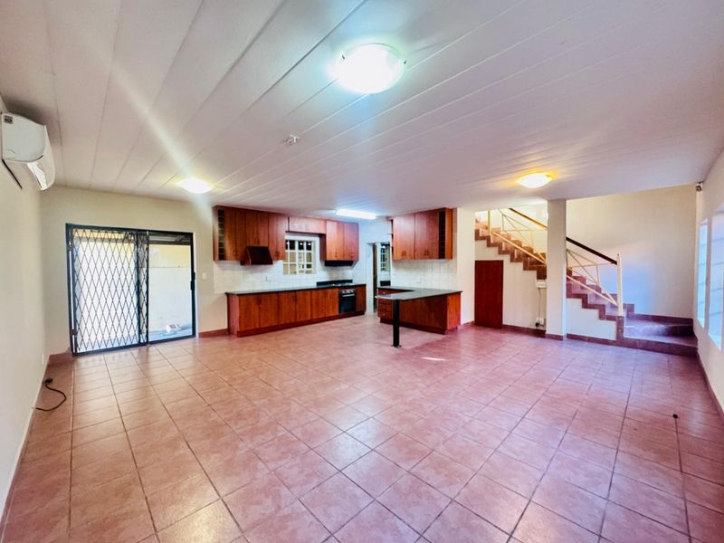 Spacious open-plan kitchen and living area featuring tiled floors, built-in wooden cabinetry, integrated appliances, and a staircase leading to the upper level.