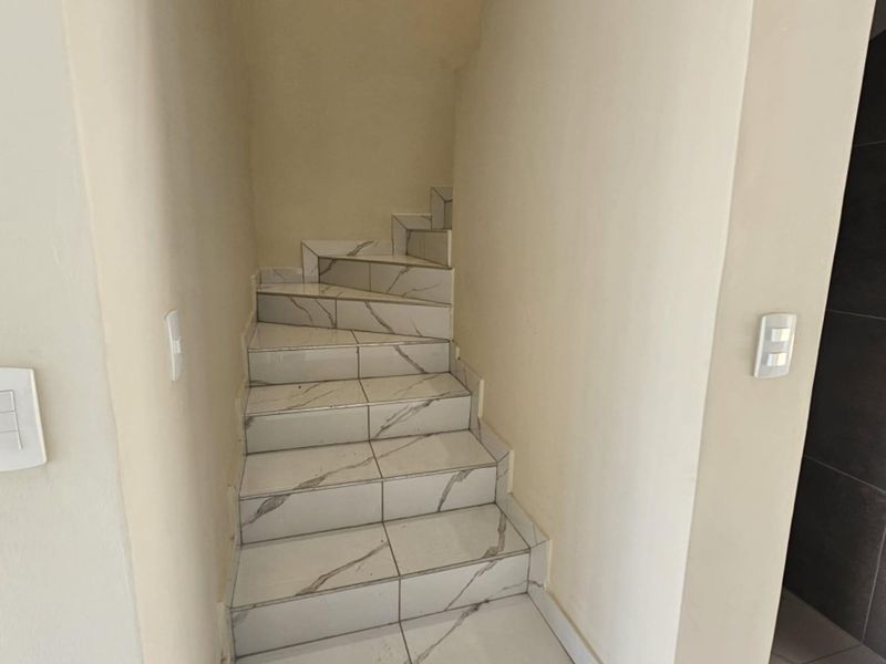 A clean, modern staircase featuring white marble-look ceramic tiles and neutral wall finishes, providing a bright and contemporary transition between levels.