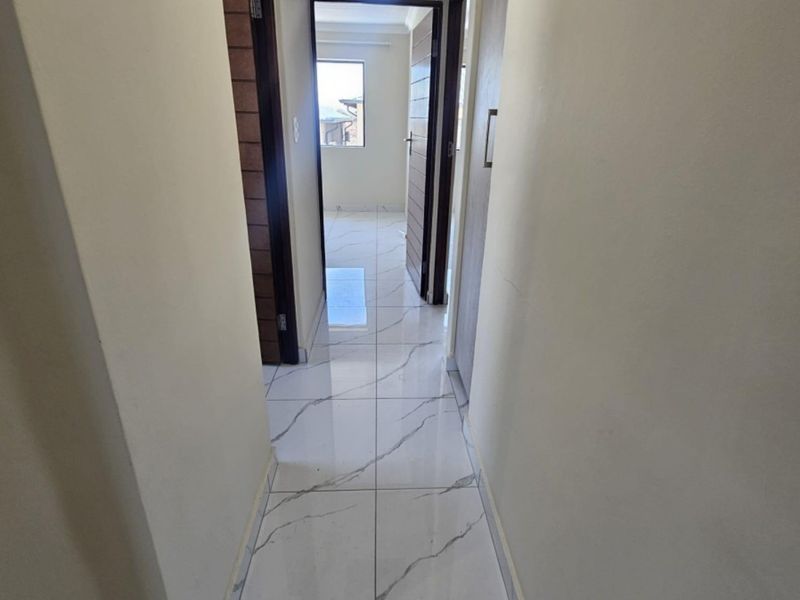 A clean, well-lit hallway featuring modern marble-look floor tiles and solid interior doors leading to adjacent rooms.