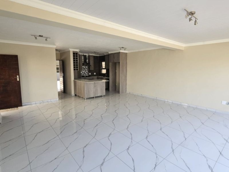 Spacious open-plan living area featuring modern marble-look floor tiles, neutral walls, and a compact, functional kitchen with built-in cabinetry and an island.