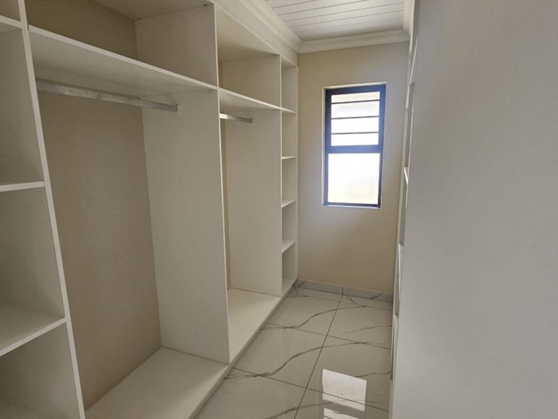 A clean, modern walk-in closet or dressing area featuring extensive built-in cabinetry, marble-look tiled flooring, and a bright window.