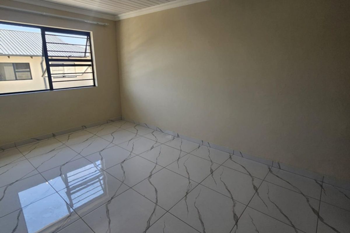 A bright, empty bedroom featuring modern marble-look tiled flooring, a white tongue and groove ceiling, and track lighting.
