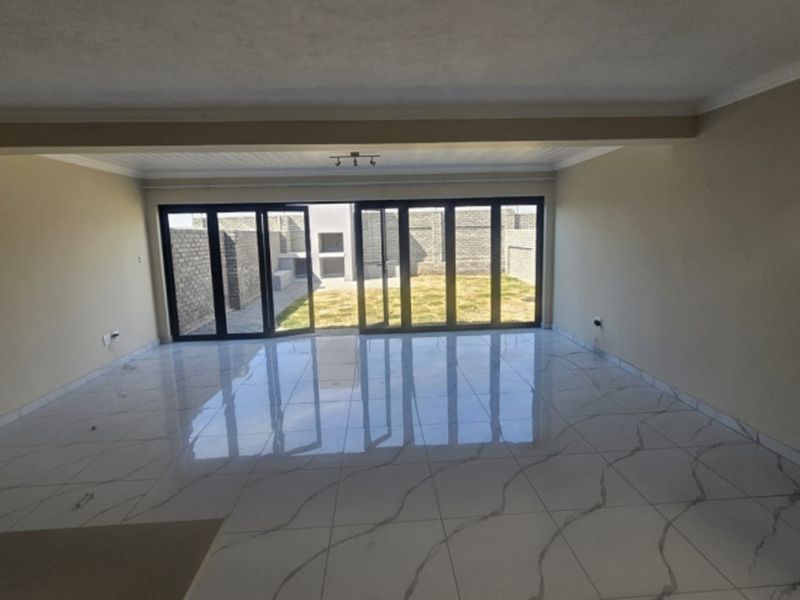 Spacious, empty living area featuring modern marble-look floor tiles and large sliding glass doors that open onto a private rear garden.