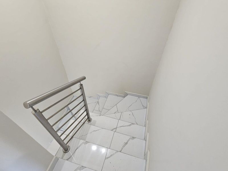 A modern staircase featuring sleek stainless steel balustrades and high-quality marble-look porcelain floor tiles.