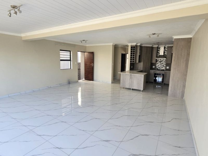 Spacious open-plan living and kitchen area featuring modern marble-look floor tiles, contemporary cabinetry, and a functional kitchen island with built-in appliances.