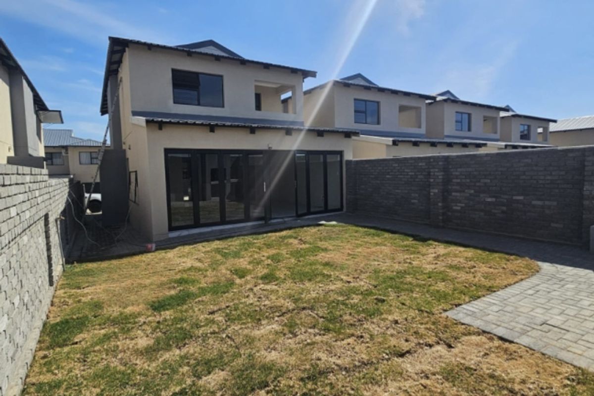 Rear view of a modern townhouse featuring a private garden, paved patio area, and large sliding glass doors leading into the living space.