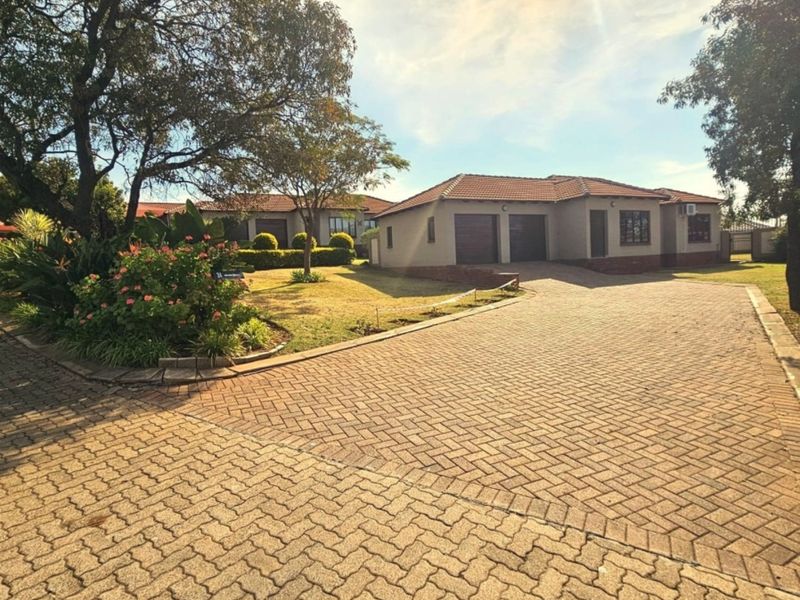 Front view of a townhouse featuring a spacious paved driveway, double garage, and well-maintained garden area under a clear sky.