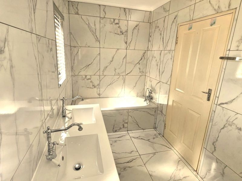 Modern bathroom featuring a double vanity, built-in bathtub, and floor-to-ceiling marble-look tiling throughout.