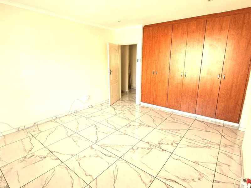 A bright, empty bedroom featuring modern marble-look tiled flooring and extensive built-in wooden cupboards.