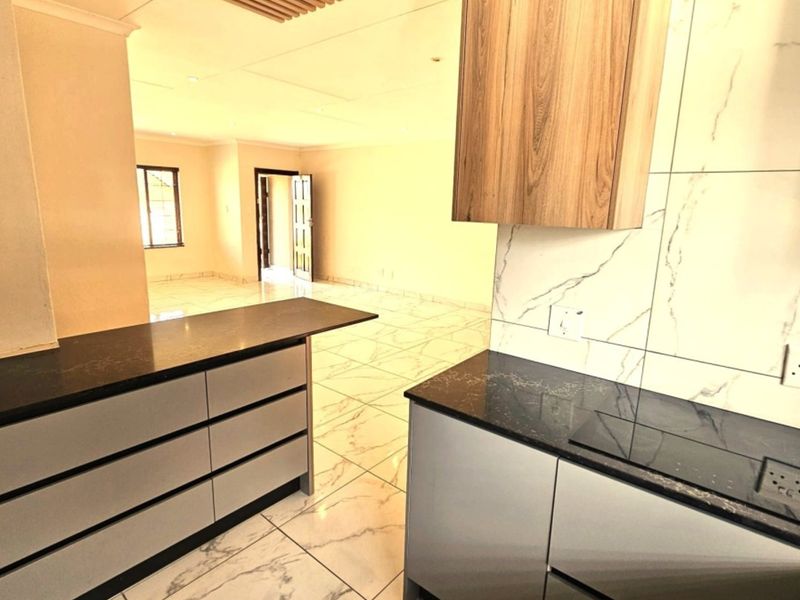 Modern open-plan kitchen and living area featuring sleek cabinetry, stone countertops, integrated hob, and contemporary marble-look tiling throughout.