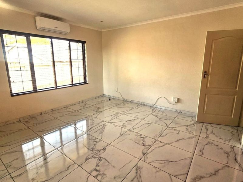 A bright, empty living room featuring modern marble-look floor tiles, a wall-mounted air conditioning unit, and recessed lighting.