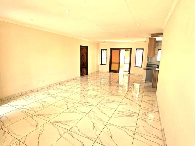 Spacious open-plan living and kitchen area featuring polished marble-look floor tiles, recessed lighting, and direct access to an outdoor space through sliding glass doors.