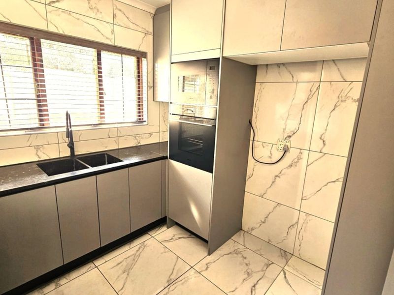 Modern kitchen featuring marble-look wall and floor tiles, fitted grey cabinetry, built-in oven and microwave, and a sleek black countertop with double sink.