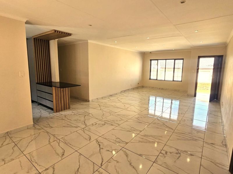 Spacious open-plan living area featuring polished marble-look floor tiles, recessed lighting, and a modern built-in breakfast bar with decorative slatted wood detailing.
