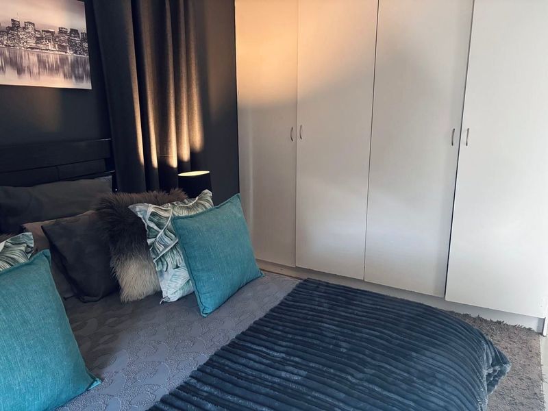A cozy bedroom featuring built-in cupboards and a dark accent wall, creating a modern and comfortable sleeping space.