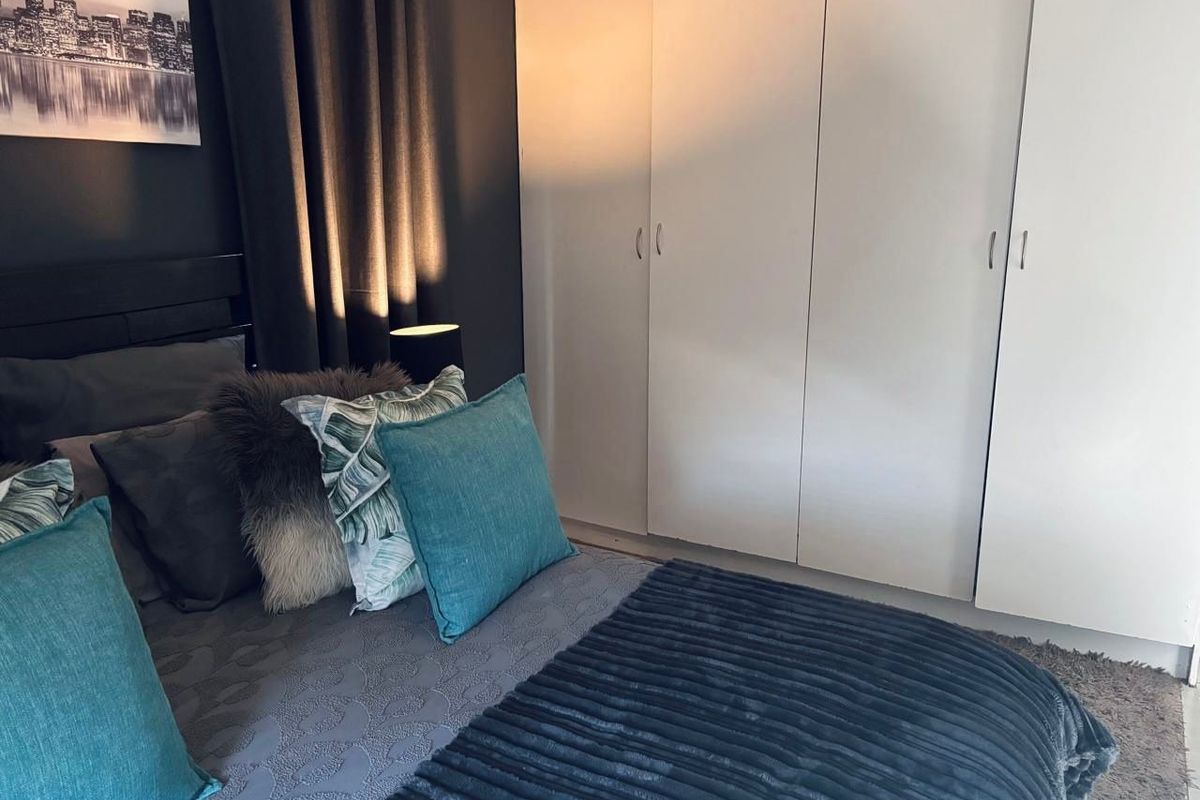 A cozy bedroom featuring built-in cupboards and a dark accent wall, creating a modern and comfortable sleeping space.